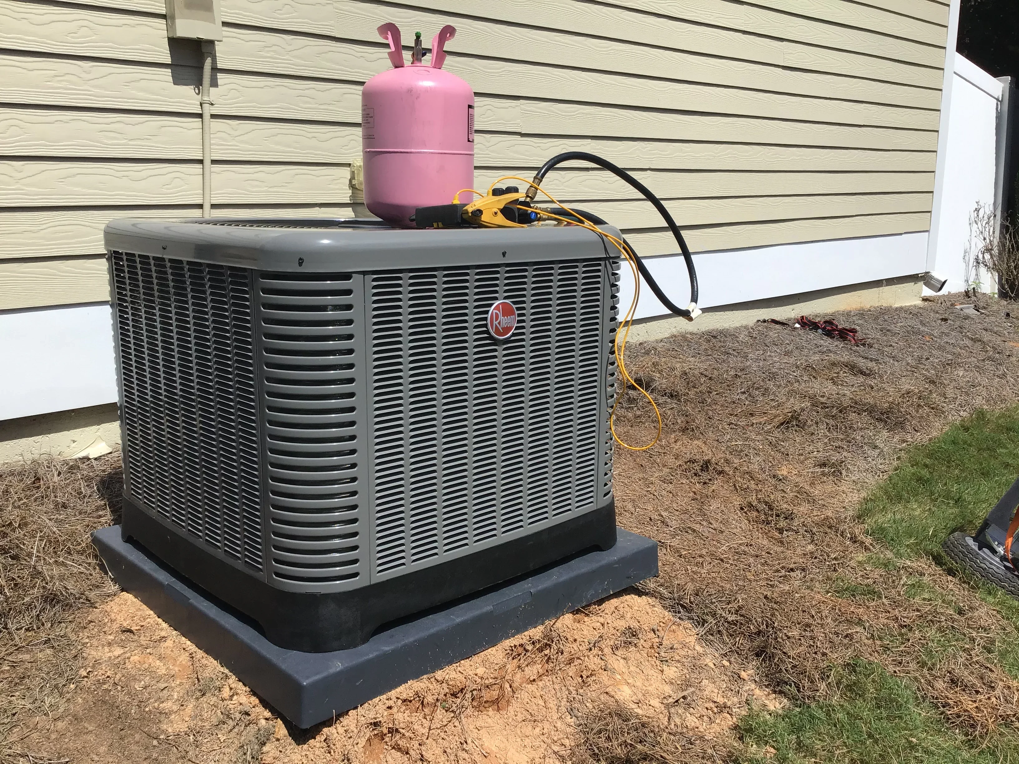 Rheem AC condenser unit on concrete pad with refrigerant lines and recovery cylinder