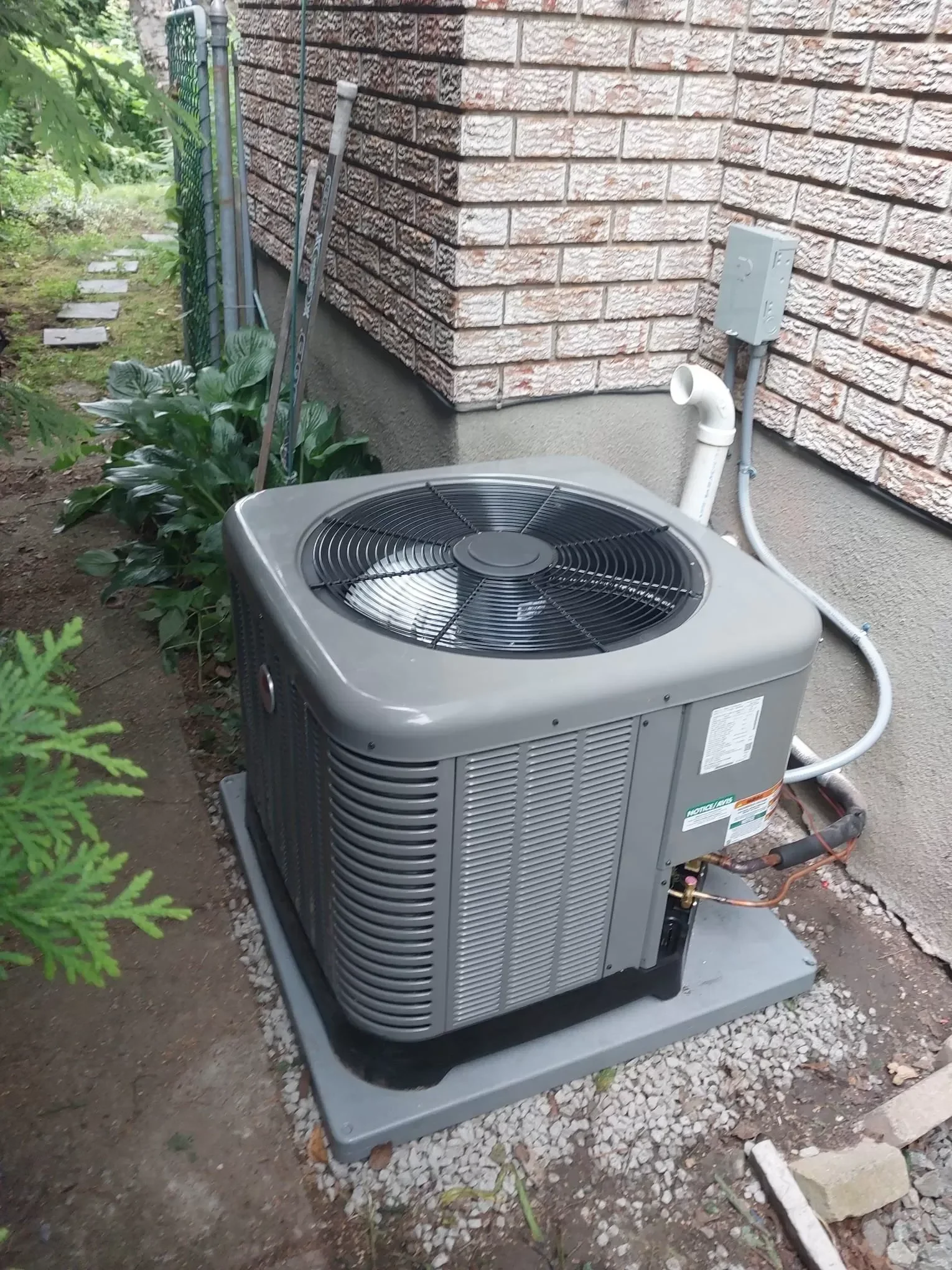 An A&K Service Inc. HVAC technician inspecting an outdoor air conditioning unit at a residential home in Alpharetta, GA. The technician checks refrigerant lines and electrical connections on a central AC system during a summer repair visit.