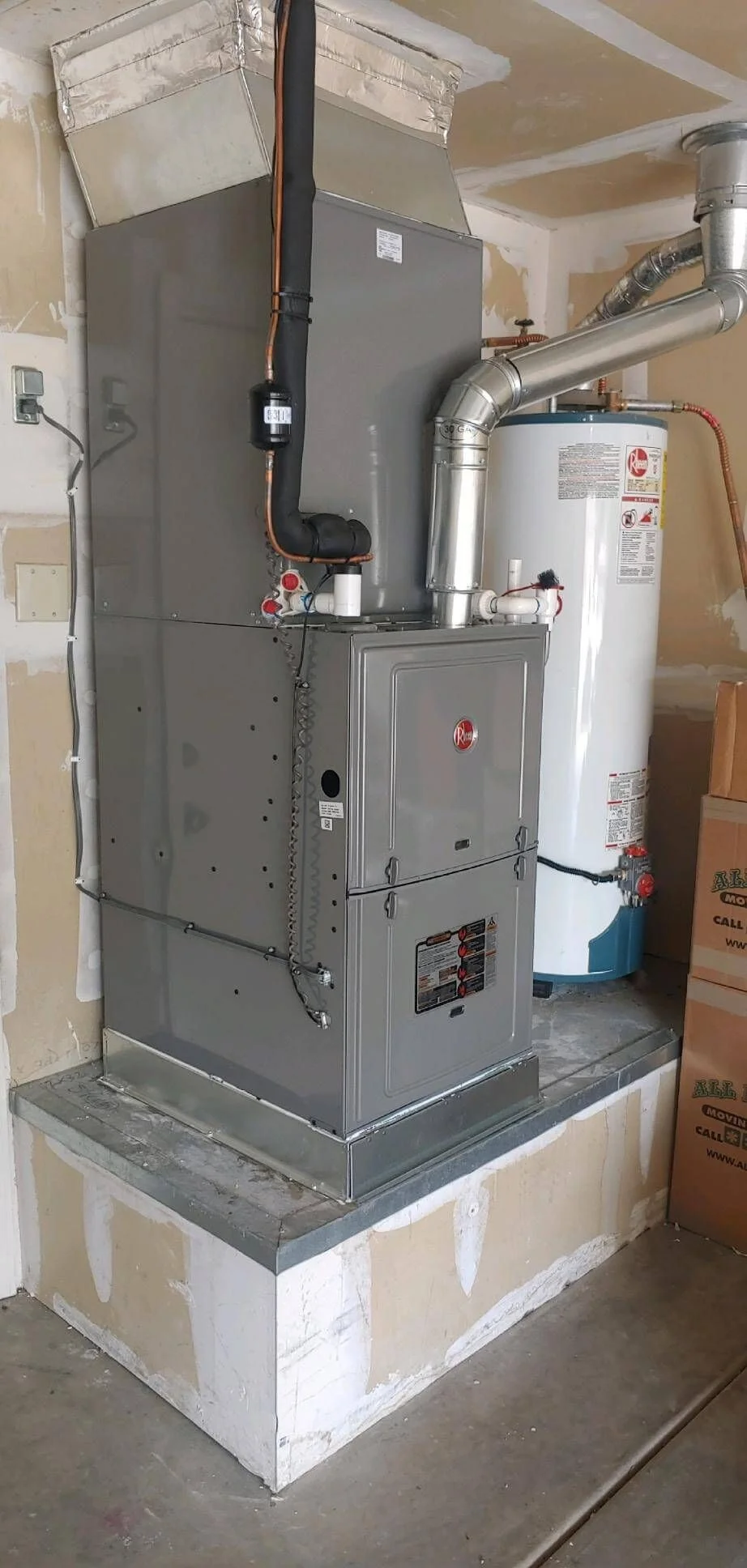 A newly installed gas furnace unit inside a residential utility room in an Alpharetta home, with fresh ductwork connections and a digital thermostat visible on the adjacent wall. An A&K Service Inc. technician performs a post-installation performance check on the system.