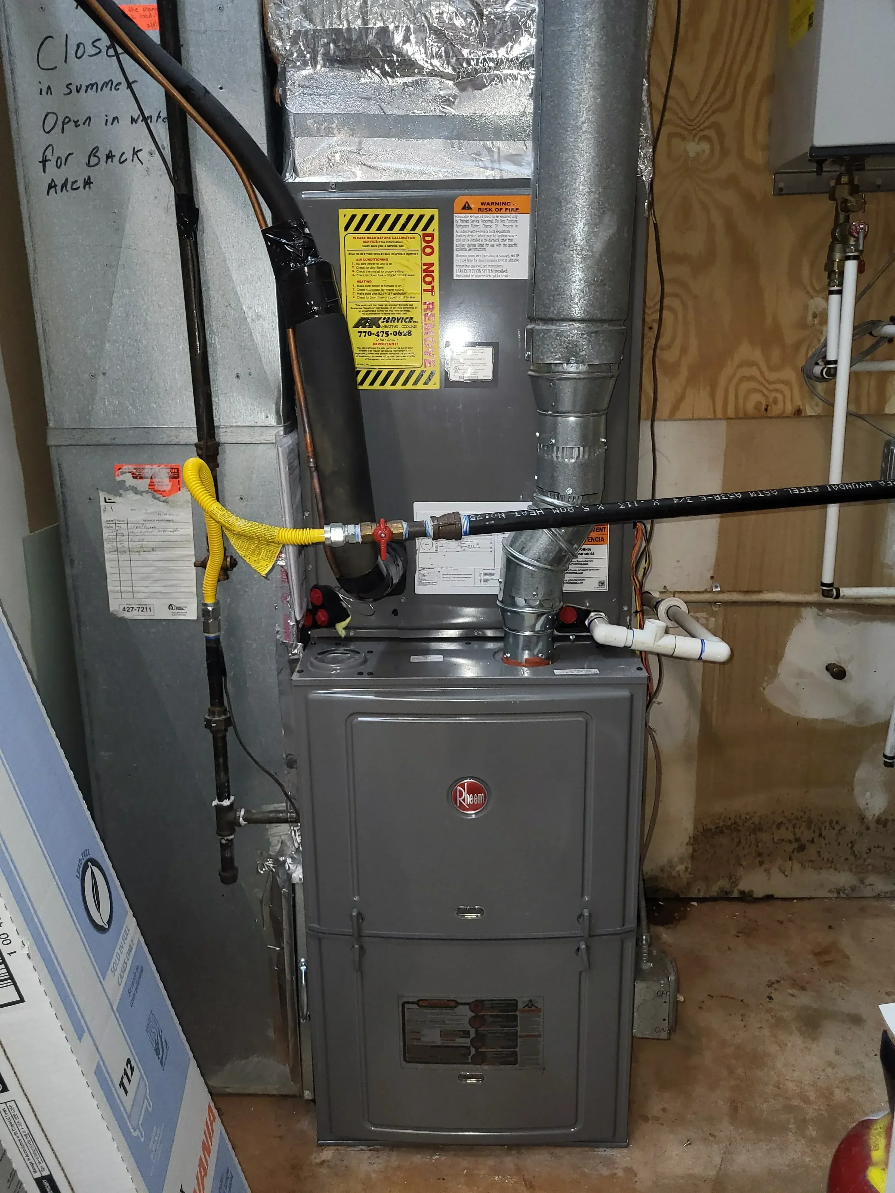 An A&K Service Inc. HVAC technician inspecting the interior components of a gas furnace inside an Alpharetta home. The technician is examining the heat exchanger and blower assembly with a flashlight during a furnace repair service call.