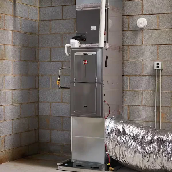 A newly installed gas furnace in an Alpharetta home utility room, with clean ductwork connections and a digital thermostat visible on the adjacent wall. An A&K Service Inc. technician reviews the system settings during the post-installation walkthrough.